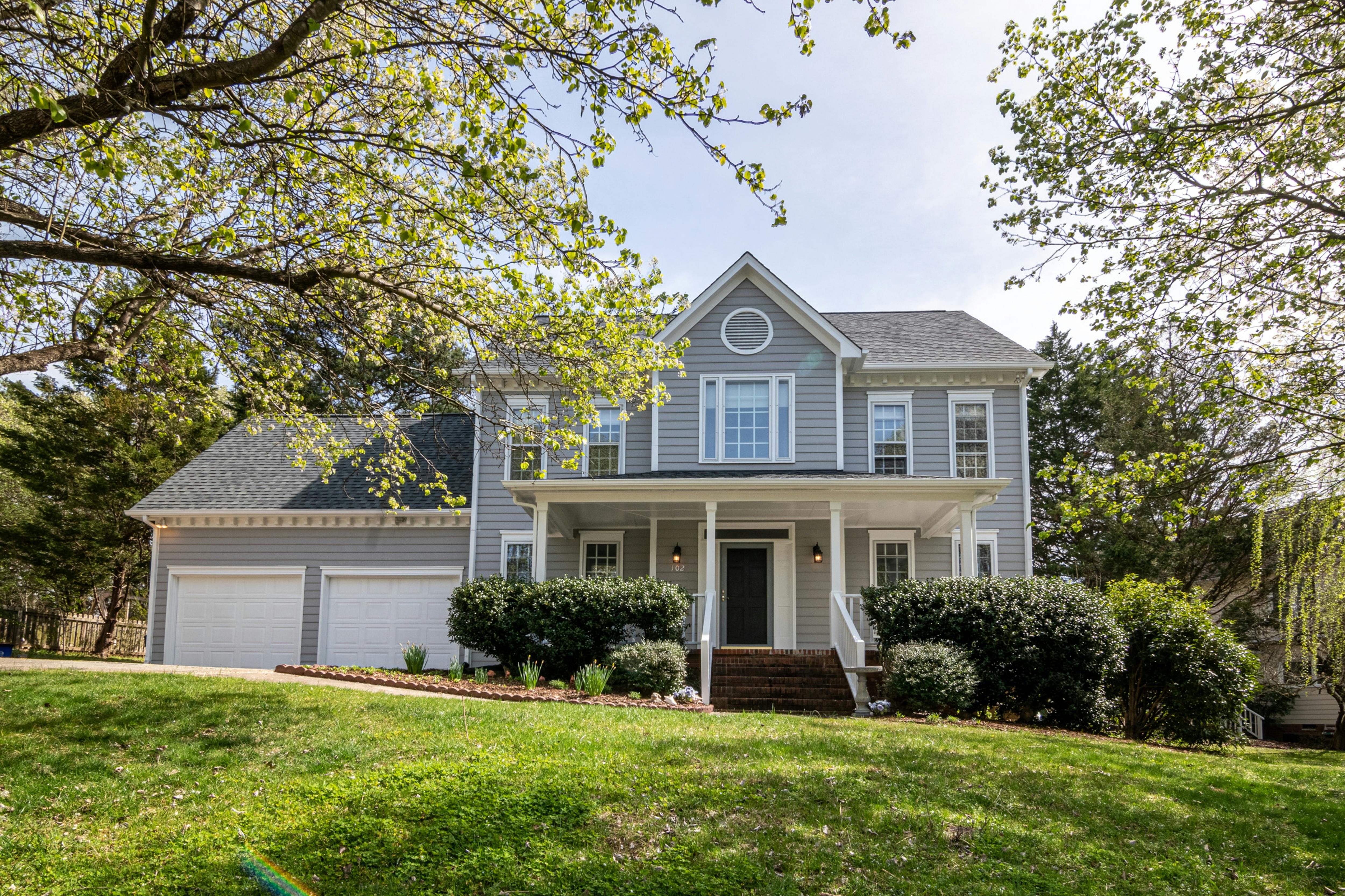 Exterior of a charming detached house with a welcoming front porch, surrounded by lush greenery and bathed in warm natural light