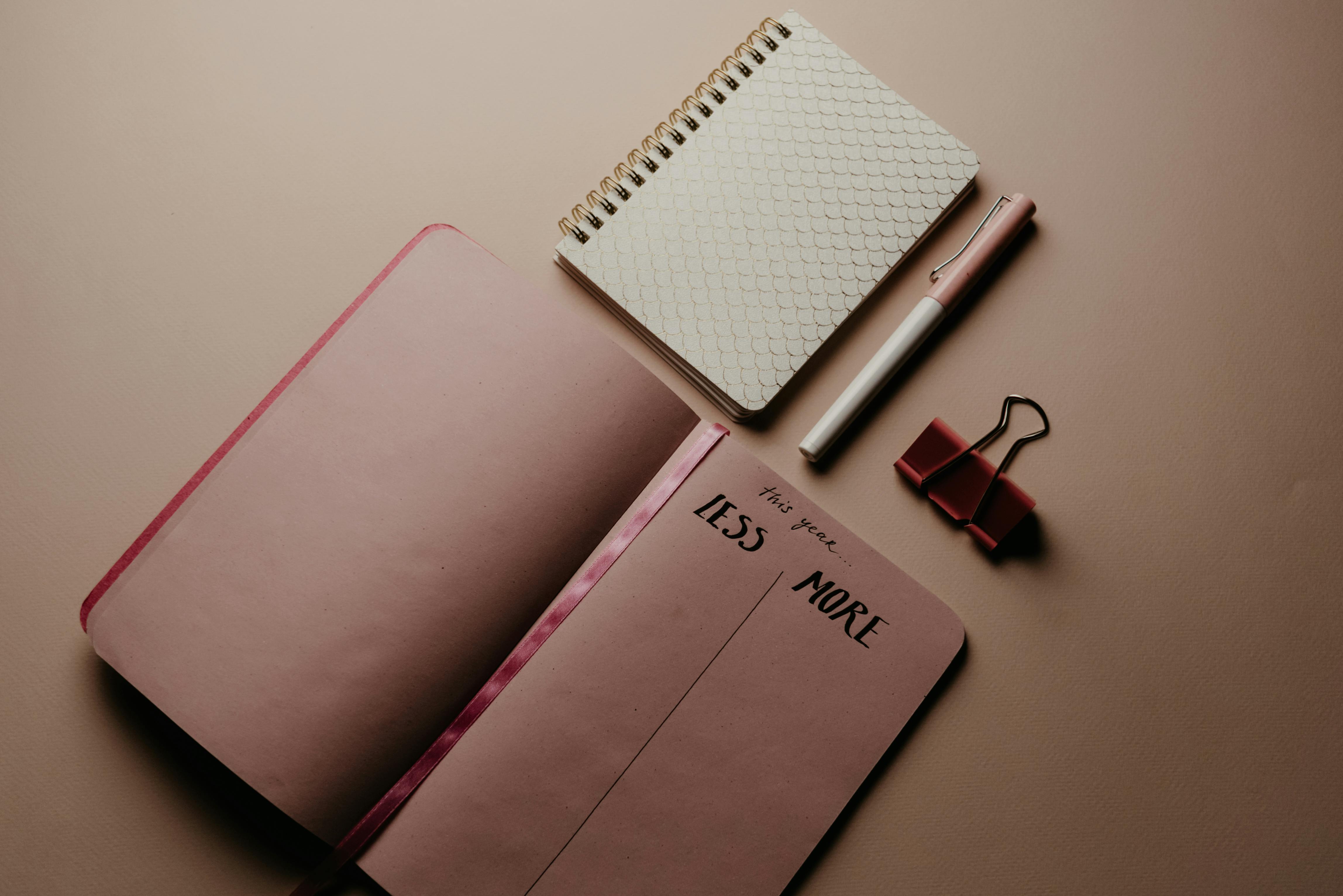 Minimalistic desk setup with an open journal, fountain pen, a bulldog clip and a small notepad