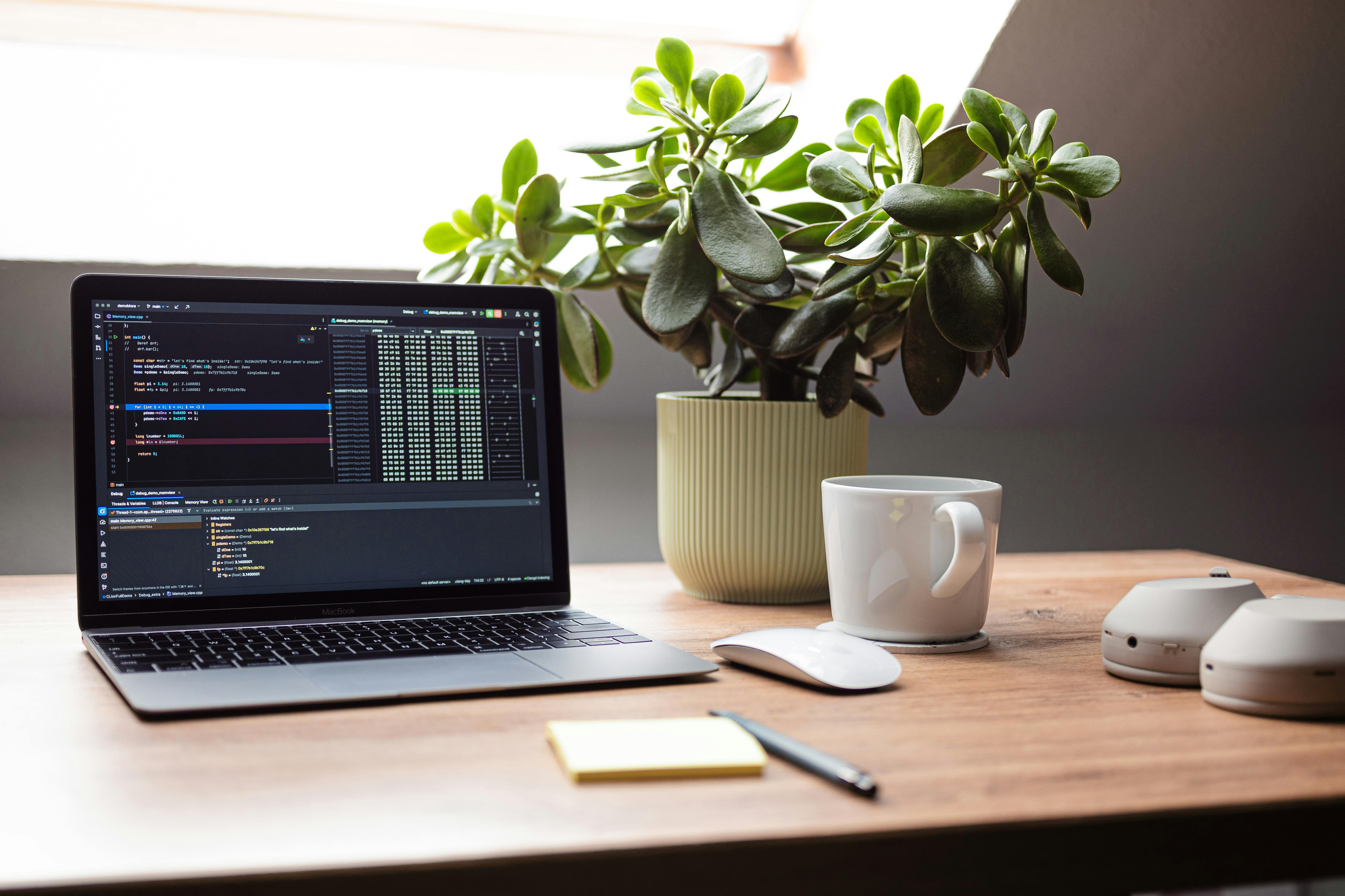Modern minimalist home office with a laptop, ceramic coffee mug, and a small green plant on a warm oak desk — representing the KG Tech Services workspace